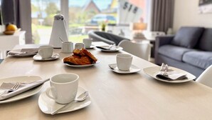 A dining table set with plates, cups, and cutlery in a modern hotel room with a view of houses and a clear sky.