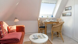 Une pièce chaleureuse avec un plafond haut, une table à manger dressée pour deux personnes, un canapé confortable et une petite table ronde sur laquelle se trouvent une tasse et une soucoupe.