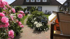 Une maison avec un toit recouvert de tuiles, un chemin en briques et un jardin où poussent des fleurs roses et blanches.