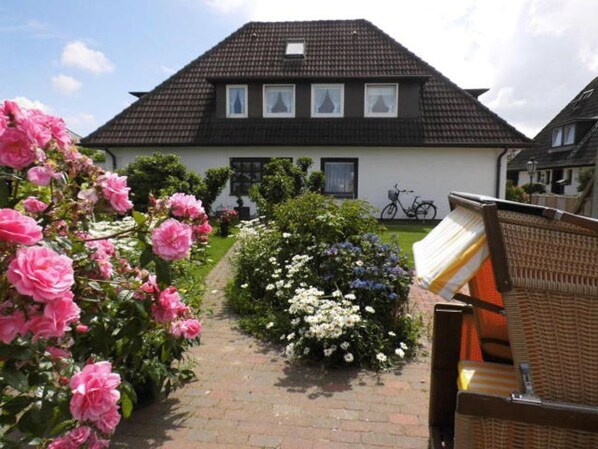 A house with a tiled roof, a brick pathway, and a garden with pink and white flowers.
