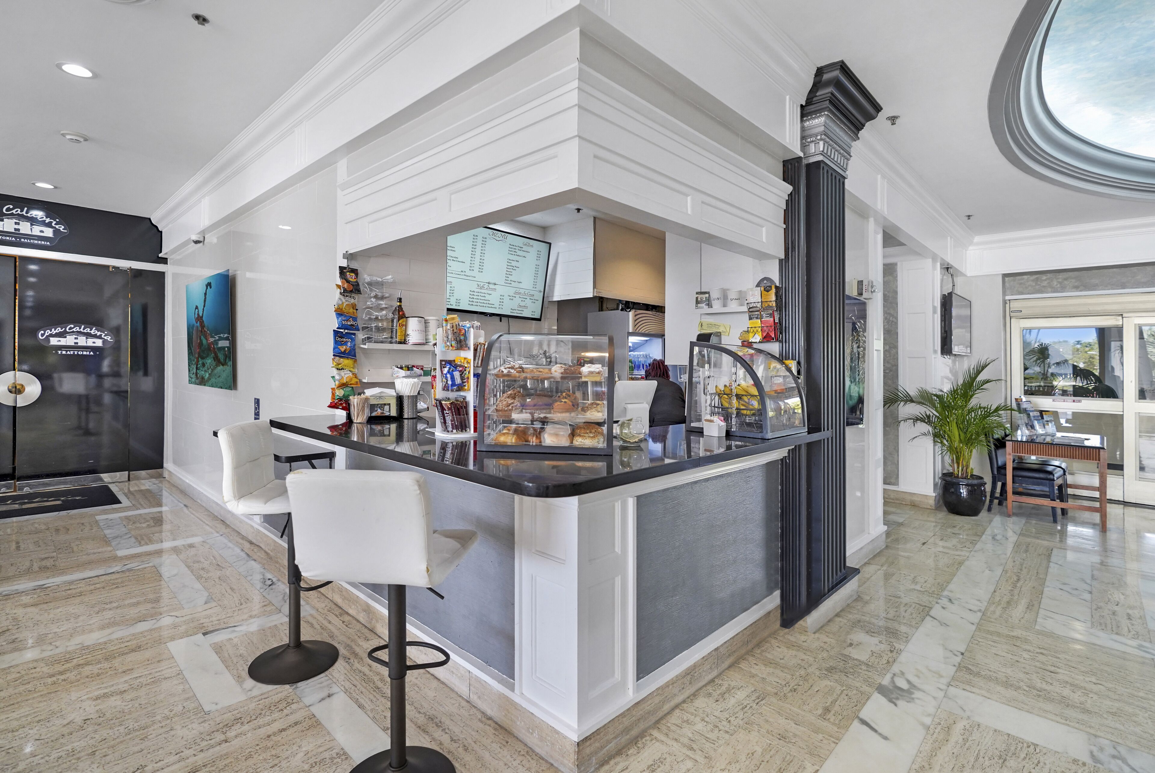 A modern cafe with a marble floor, white bar stools, a menu display, and a potted plant.