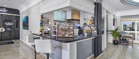 A modern cafe with a marble floor, white bar stools, a menu display, and a potted plant.