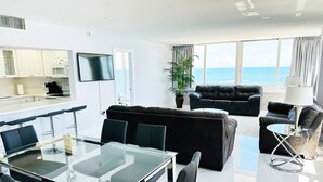A modern living room with a glass dining table, black leather sofas, and a large window with a view of the sea. - Beachfront condo-We are on the Beach-Views every window-Patio Pool-No resort fee (Fort Lauderdale)