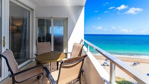 A balcony with a table and chairs, overlooking a beach with clear blue water and a few people in the distance. - Beachfront condo-We are on the Beach-Views every window-Patio Pool-No resort fee (Fort Lauderdale)