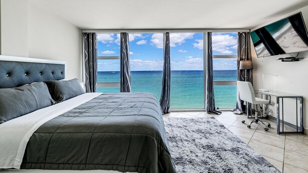 A bedroom with a large bed, a desk, and a TV. - Beachfront condo-We are on the Beach-Views every window-Patio Pool-No resort fee (Fort Lauderdale)