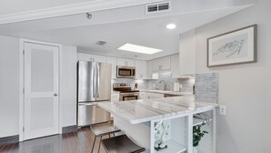 A modern kitchen with white cabinets, stainless steel appliances, a marble island, and a framed artwork on the wall.