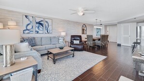 A spacious living room with a sofa, coffee table, and chairs, a dining area with a table and chairs, and a kitchen with a refrigerator.