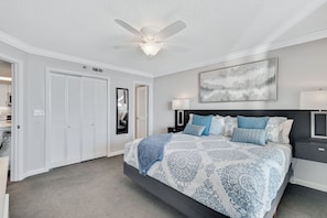 A bedroom with a bed, a ceiling fan, a nightstand, a lamp, a painting, and a closet.