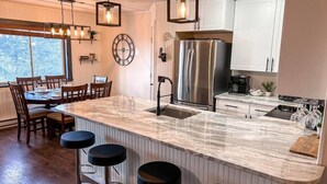 A modern kitchen with a marble island, stainless steel appliances, and a dining area with wooden chairs.