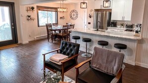 A modern kitchen with a central island, bar stools, and a dining area with a clock on the wall.