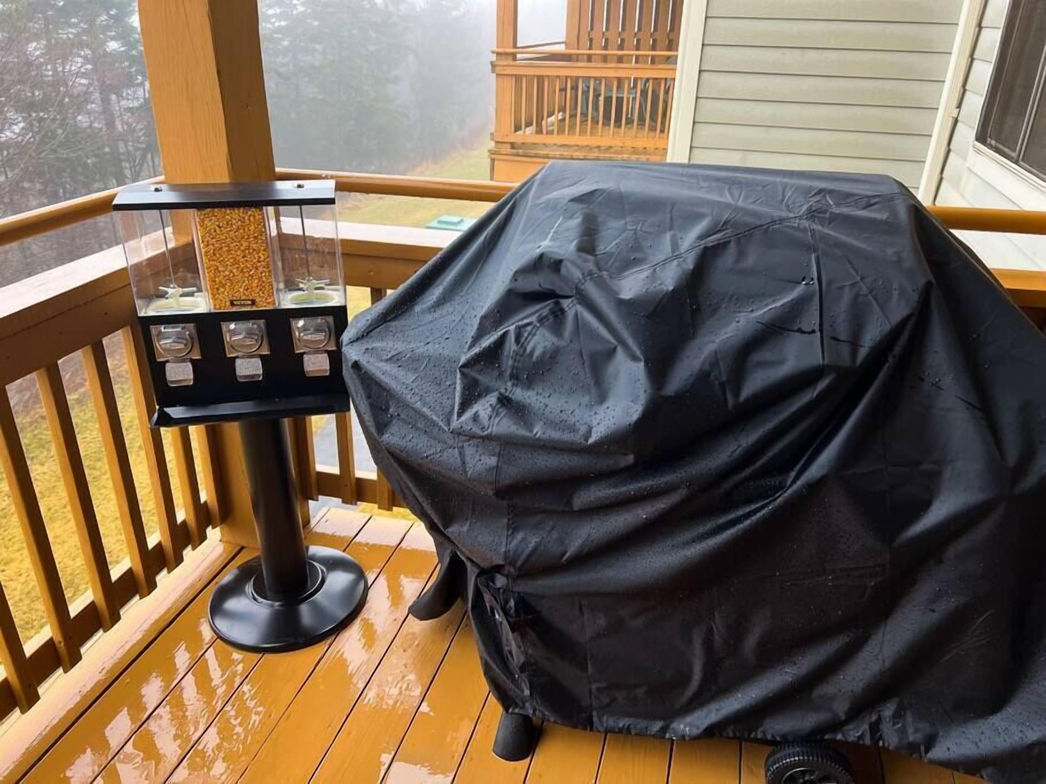 A covered grill on a wooden deck with a pellet stove and a window in the background.