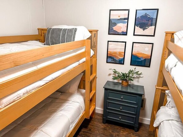 A room with two bunk beds, a small dark dresser, and four framed landscape paintings on the wall. - Modern Snowshoe Retreat - 3BR/2BA - Walk to Slopes + Mountain Views (Snowshoe)