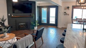 A modern living room with a fireplace, a television, and a dining area with a bar.