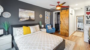 Een moderne slaapkamer met een bed, nachtkastjes, een blauwe stoel, een plafondventilator en een houten deur.