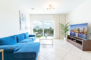 A modern living room with a blue sofa, a flat-screen TV, and a large window with a city view.