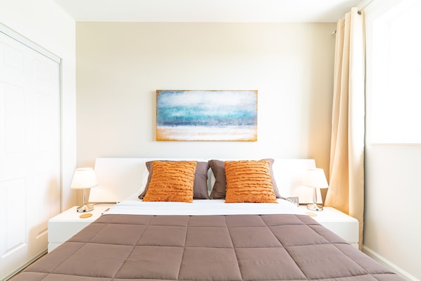 A neatly arranged hotel room with a large bed, two pillows, two bedside tables with lamps, and a painting on the wall.