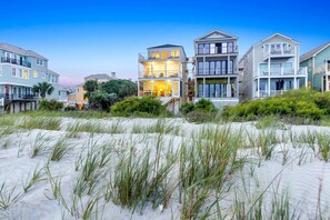A beachfront property with multiple-story houses featuring balconies, a sandy beach, and coastal vegetation.