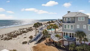 Une propriété située en bord de mer, comprenant un bâtiment à deux étages, une piscine et une zone de plage agrémentée de palmiers.