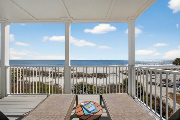 A covered balcony with a view of the beach and ocean.