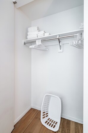 A white bathroom with a wooden floor, a white laundry basket, and a metal towel rack with folded towels.