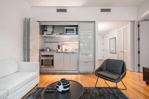 Un salon moderne avec un canapé blanc, une table basse noire sur laquelle se trouvent une télécommande et un vase, et un fauteuil gris.