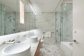 Un baño moderno con un espejo grande, dos lavamanos, un inodoro y una zona de ducha con mampara de vidrio.