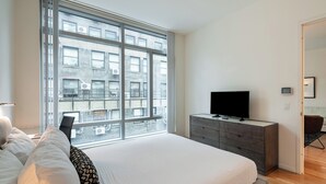 Una camera da letto moderna con una grande finestra, un letto, una cassettiera e una televisione.