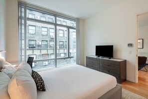 Un dormitorio moderno con una ventana grande, una cama, un aparador y un televisor.