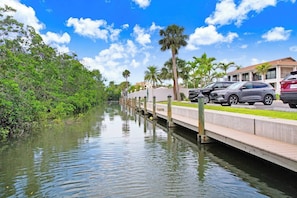 A canal with a pedestrian bridge, lined with palm trees and parked cars.