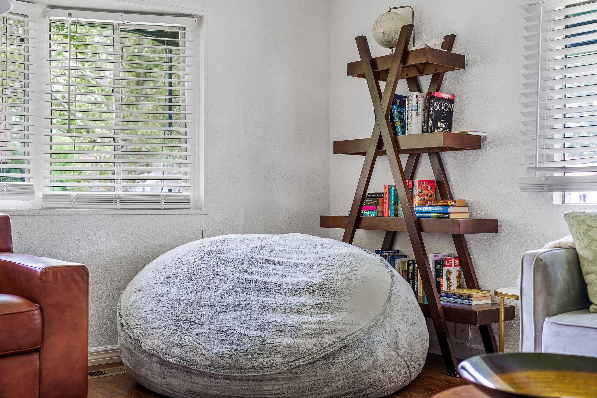 A cozy reading nook with a bean bag chair, a wooden ladder bookshelf, and a window with blinds.