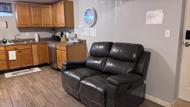 A living room with a leather sofa, wooden cabinets, a kitchen area, and a clock on the wall. - 1 BRM Basement Apartment/ 420 friendly outside (Lakewood)