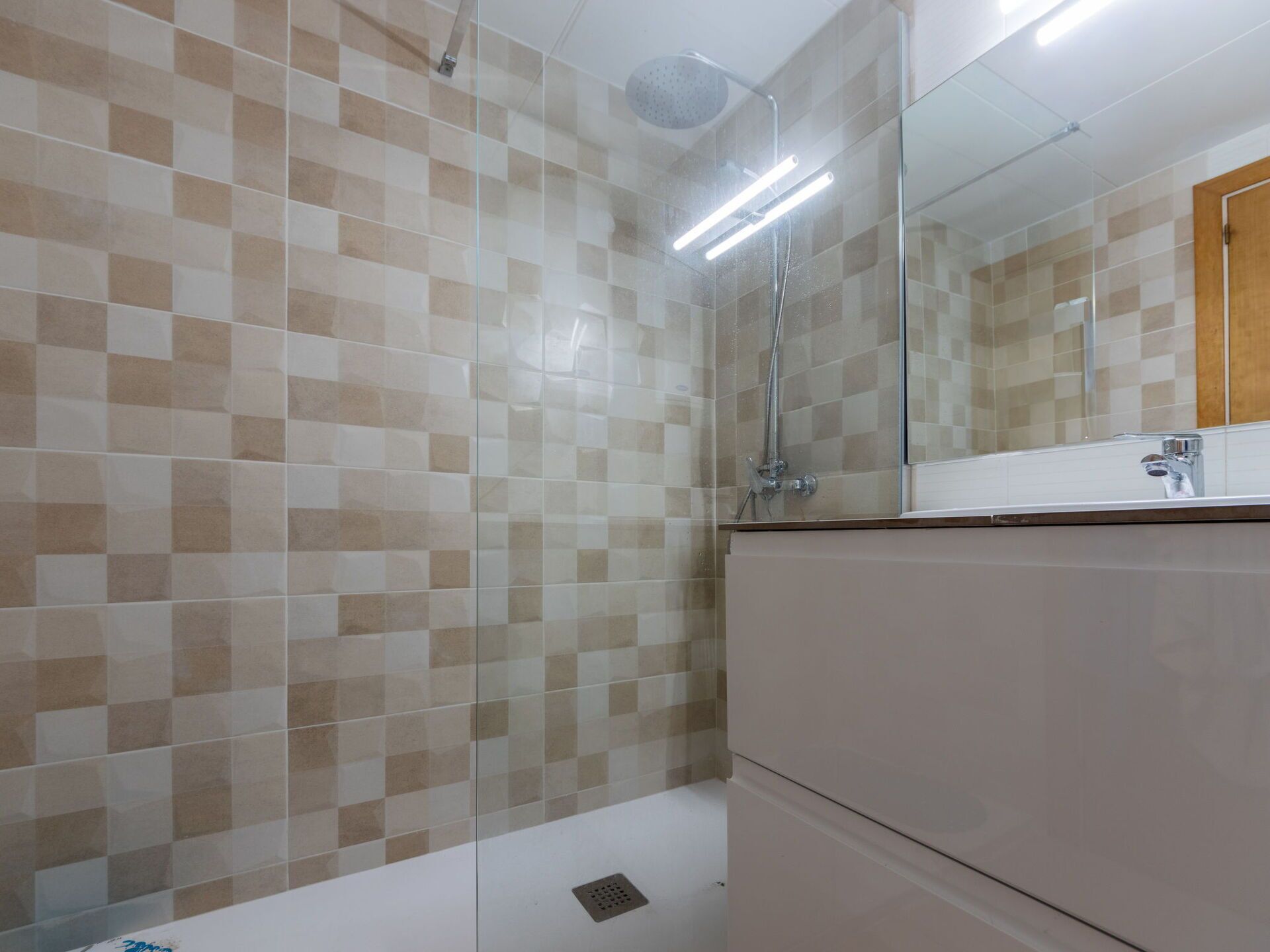 Ein Badezimmer mit Schachbrettmuster-Fliesen an den Wänden, einer Glasdusche und einem Spiegel über dem Waschbecken.