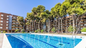 Una piscina con agua azul cristalina, rodeada de árboles y un edificio de varios pisos con balcones.