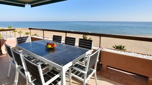 Un espacio de estar techado al aire libre con una mesa y sillas, con vista a una playa.