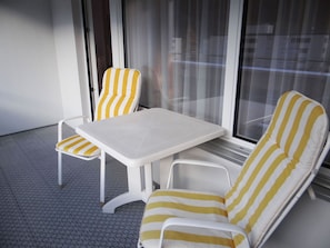 A balcony with a white table and two striped chairs.