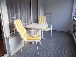 A small room with two striped chairs and a white table, a window with curtains, and a patterned floor.