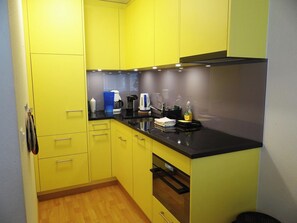 A compact kitchen with yellow cabinets, a black countertop, and basic appliances including a coffee maker and kettle. - Sunnmatt West Wohnung 744 Appartement/Fewo 2-Bettwohnung by Interhome (Engelberg)