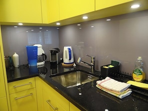 A modern kitchen with yellow cabinets, a stainless steel sink, a coffee maker, a kettle, and a dish soap bottle.