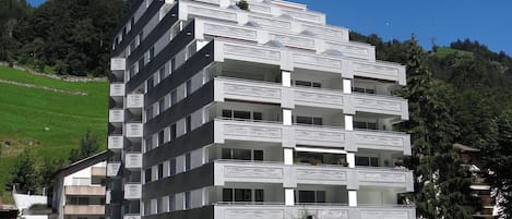 Um edifício de vários andares com varandas, uma área de estacionamento e uma escultura em primeiro plano.