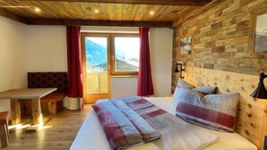Ein Schlafzimmer mit einem hölzernen Kopfteil, einem Bett mit einer gestreiften Decke, einer Bank und Blick auf Berge durch ein Fenster.