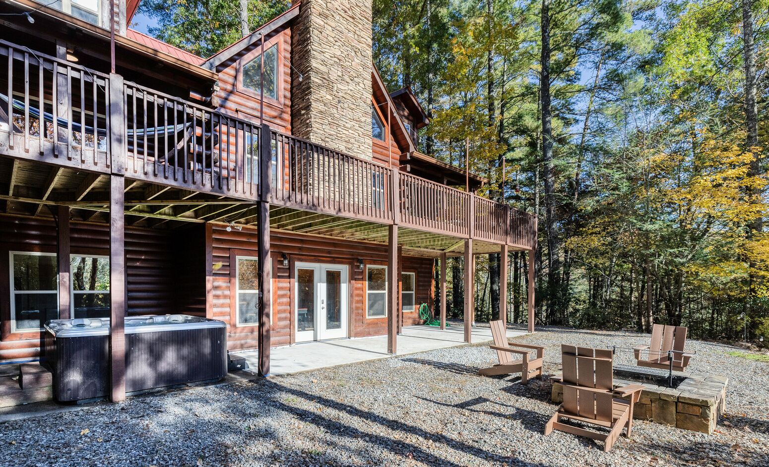 Une cabane en rondins dotée d’un balcon, d’un jacuzzi et d’un espace extérieur aménagé, le tout entouré d’arbres.