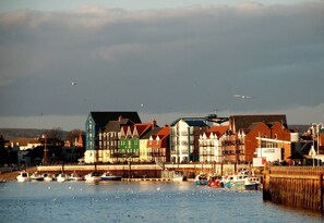 A waterfront town with colorful buildings, boats docked along the shore, and a wooden pier extending into the water. - Seafront Apartment Private Garden & Free Parking (Littlehampton)