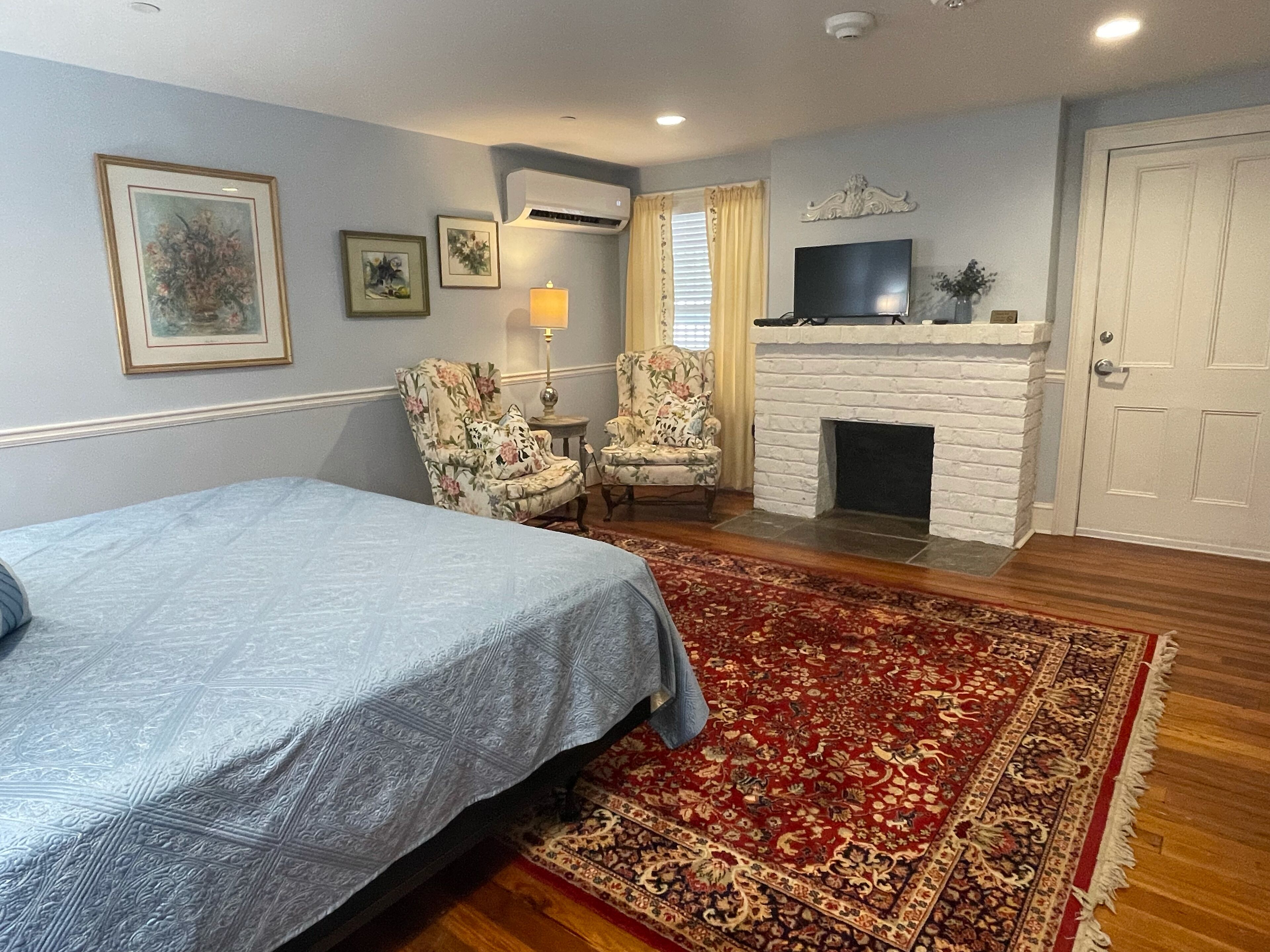 A bedroom with a bed, two chairs, a fireplace, and a TV.