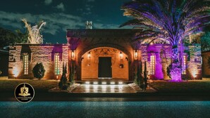 A hotel entrance with a brick archway, illuminated by purple lighting, and a palm tree to the right. - 🛡Medieval Castle Hôtel ™ (McAllen)