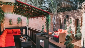 An outdoor patio with a red sofa, wicker furniture, and a brick wall backdrop. - 🛡Medieval Castle Hôtel ™ (McAllen)