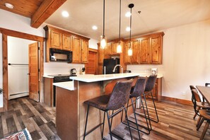 A kitchen with wooden cabinets, a stainless steel refrigerator, a microwave, and a bar stool seating area.