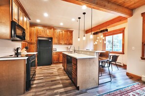 A modern kitchen with wooden cabinets, a black refrigerator, and pendant lighting.