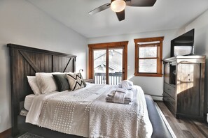 A bedroom with a bed, a ceiling fan, a window, and a TV.