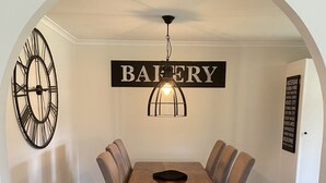A dining area with a wooden table and chairs, a wall clock, and a sign reading "BAKERY". - Farm stay with alpacas at your doorstep (Cromer)
