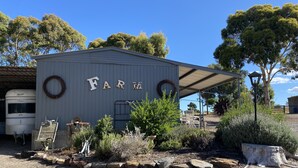A rustic farm building with the word "FARM" on the side, surrounded by greenery and a parked camper. - Farm stay with alpacas at your doorstep (Cromer)
